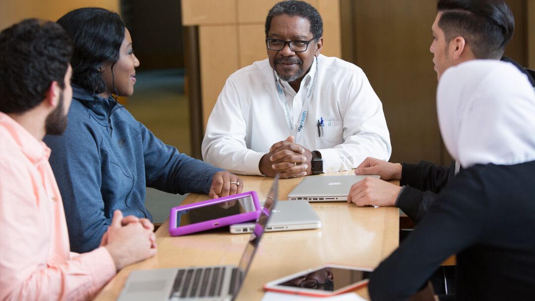 Dean Talmadge King sits at a conference table with medical students on either side of him