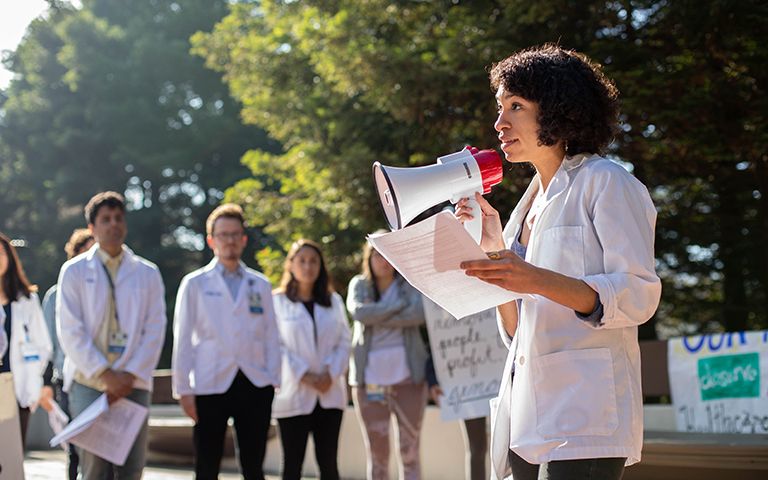 Sheyda Aboii speaks to her fellow medical students, including, background left to right, Arun Burra, Andrés Calvillo and Avery Thompson and the community, at a White Coats for Black Lives (WC4BL) Teach-in, which set out to “model an explicitly anti-racist healthcare education that elevates queer, disabled, formerly criminalized, and undocumented people of color in the communities and hospitals within which we work,” on the 4th anniversary of WC4BL in 2018