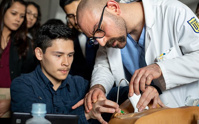 Masis Isikbay, MD, right, resident in the department of Surgery, assists Jonathan Cornejo in using ultrasound to place a central line or IV in a simulation dummy