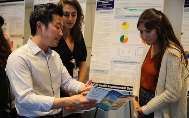 Medical students (from left) Daniel Kim, Anna Grandis and Maria Castro display their clinical microsystem clerkship project at a symposium on Nov. 18, 2019.