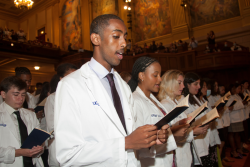 Students standing in white coats read from booklet