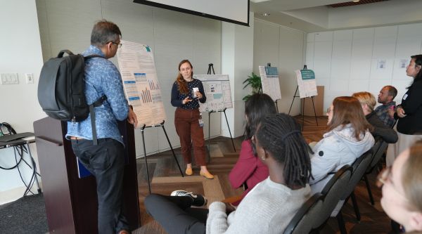 Student standing next to scientific poster gives a presentation at the 2024 Inquiry Symposium as an audience watches